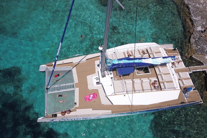 A white catamaran anchored over pale sand with swimmers off the stern