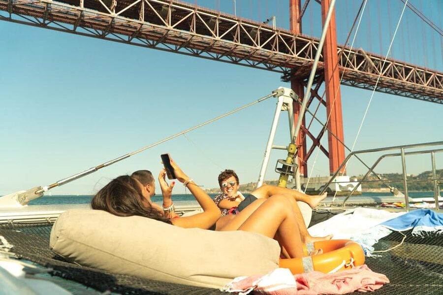 Lisbon: Catamaran Boat Party with Music, Open Bar & Dives - A party boat with Lisbon scenery in the background